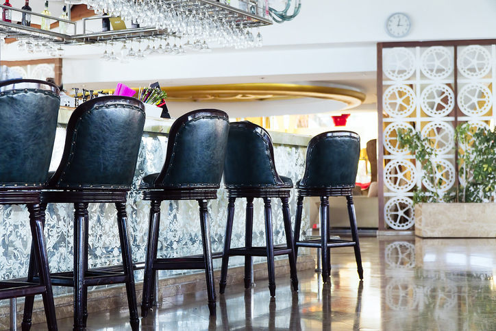 A row of beautifully designed bar stools sit in front of a bar, waiting to provide comfort for customers.