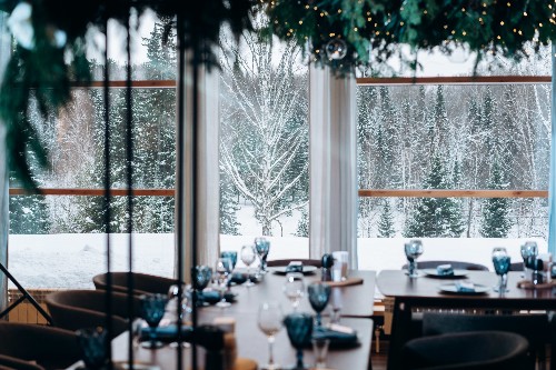 Restaurant tables are set for guests while snow is on the trees outside.